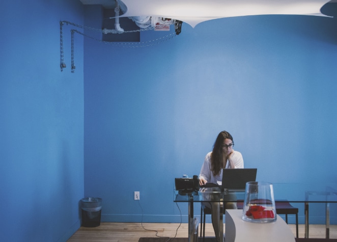 femme travaille sur un ordinateur à un bureau en verre dans une chambre bleue