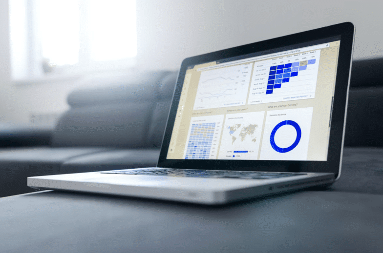 Laptop deschis către un tablou de bord cu statistici pe o canapea