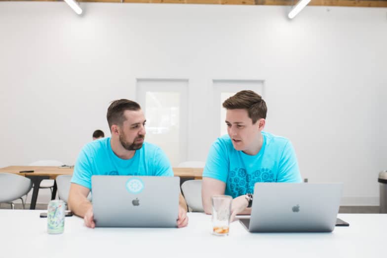 deux hommes en chemises bleues collaborent sur leurs ordinateurs portables dans une salle blanche