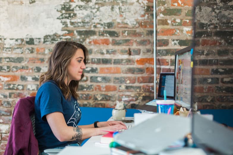 uma mulher trabalha em um computador em frente a uma parede de tijolos