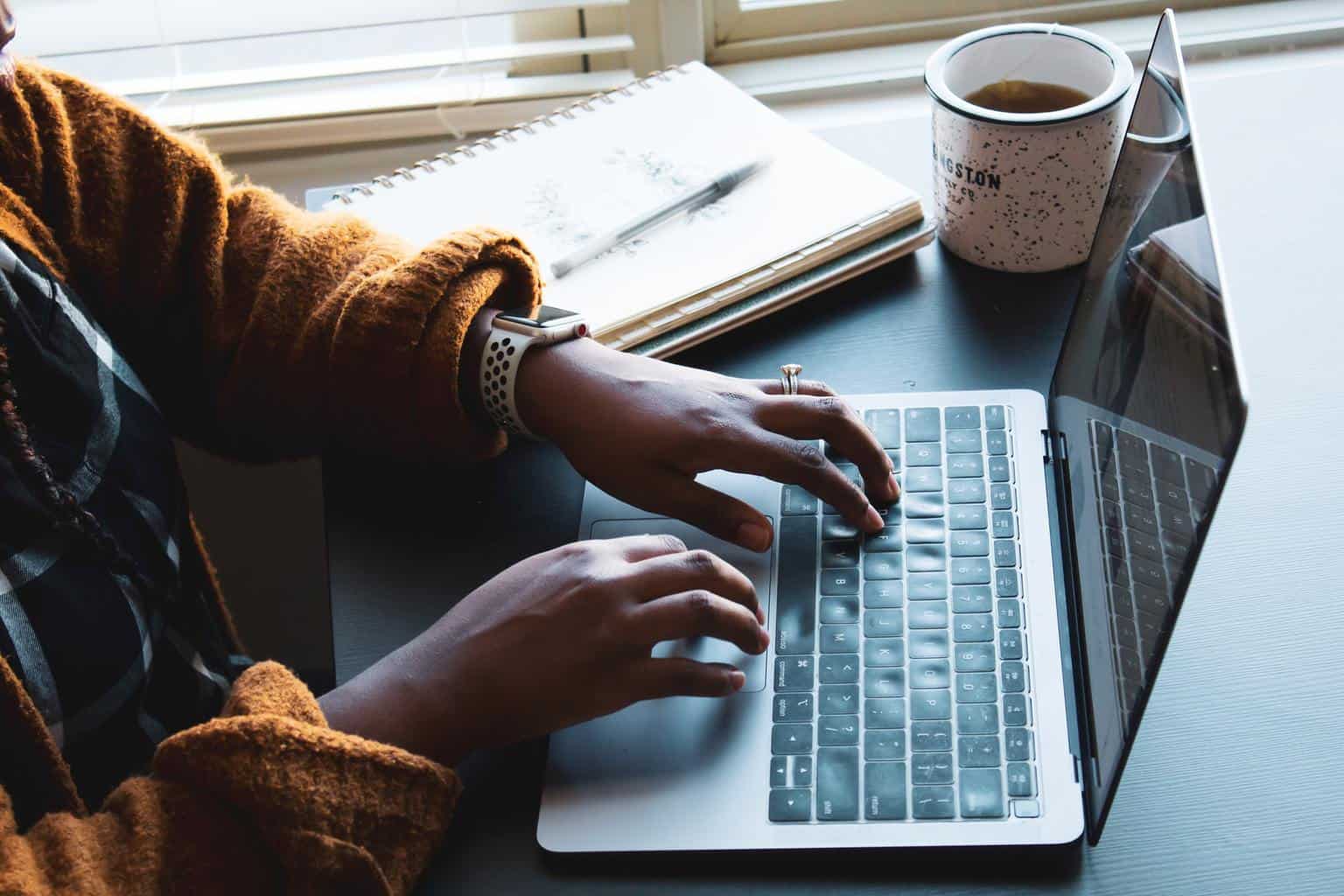 Mit Kaffee am Laptop tippen