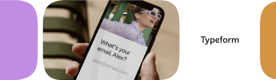 Primer plano de una mano que sostiene un teléfono inteligente que muestra una pregunta interactiva "¿Cuál es tu correo electrónico, Alex?" con una figura borrosa en el fondo con gafas de laboratorio, junto al logotipo de Typeform, enfatizando una experiencia de usuario personalizada en formularios en línea.