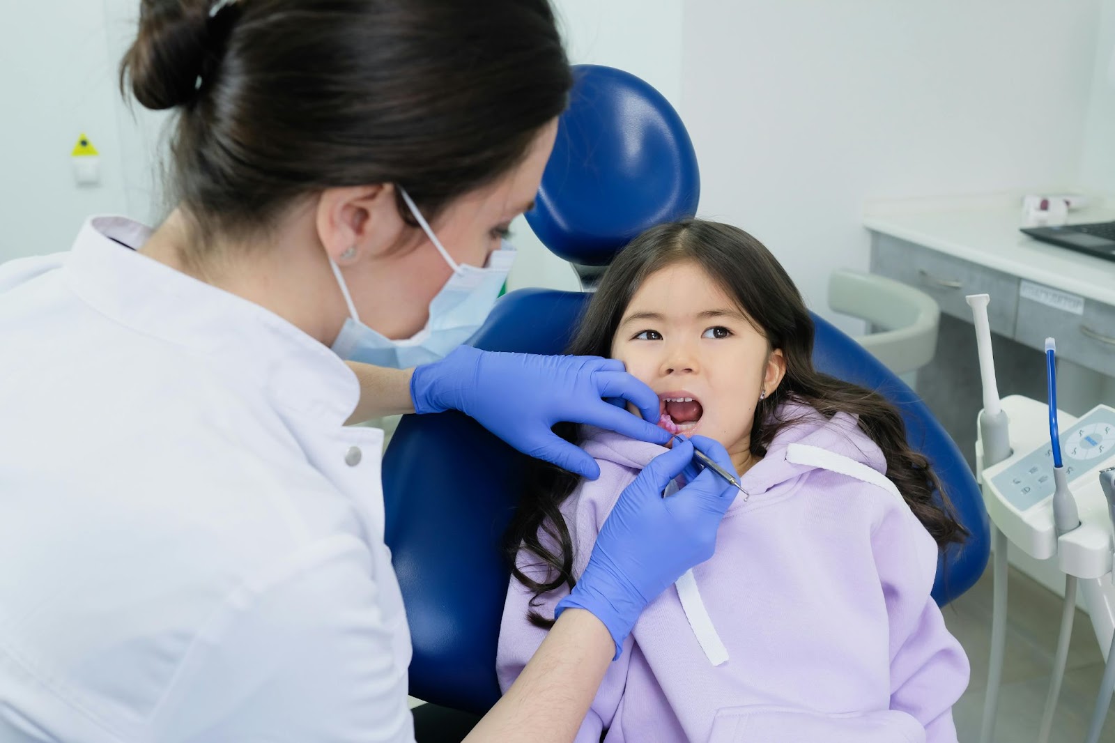 Higienista dental limpiando delicadamente los dientes del niño en una silla azul.