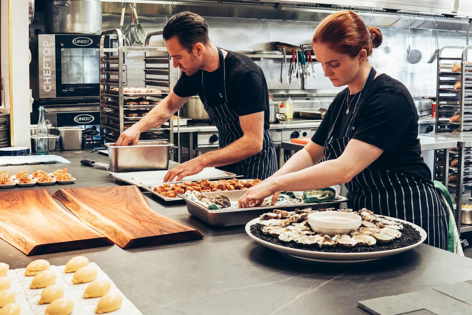 Dois chefs preparando bandejas de comida para o que parece ser uma grande festa ou algum tipo de evento.