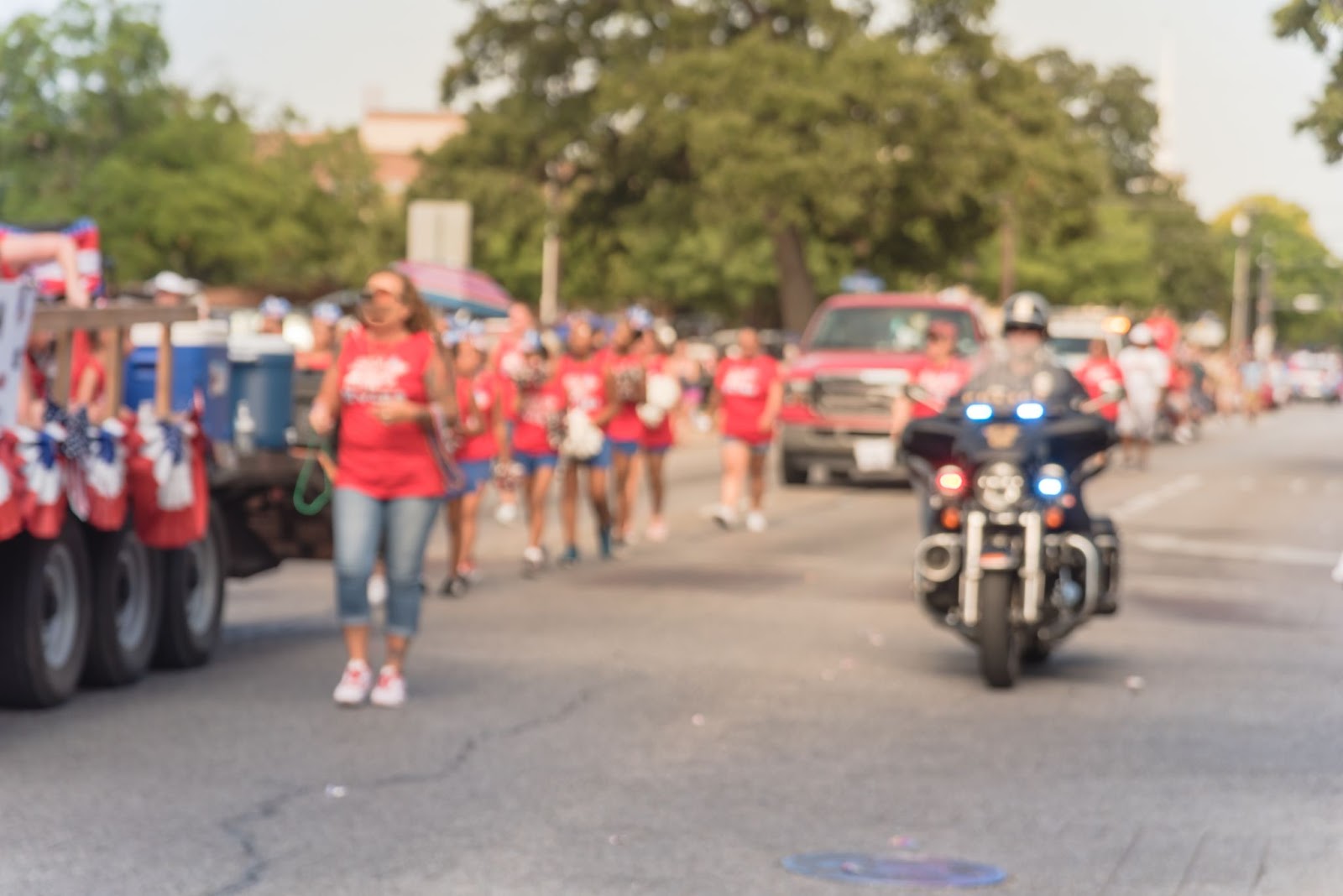 Image floue d'un défilé du 4 juillet où tout le monde porte des chemises rouges et des pantalons bleus tandis qu'un policier à moto roule à ses côtés.