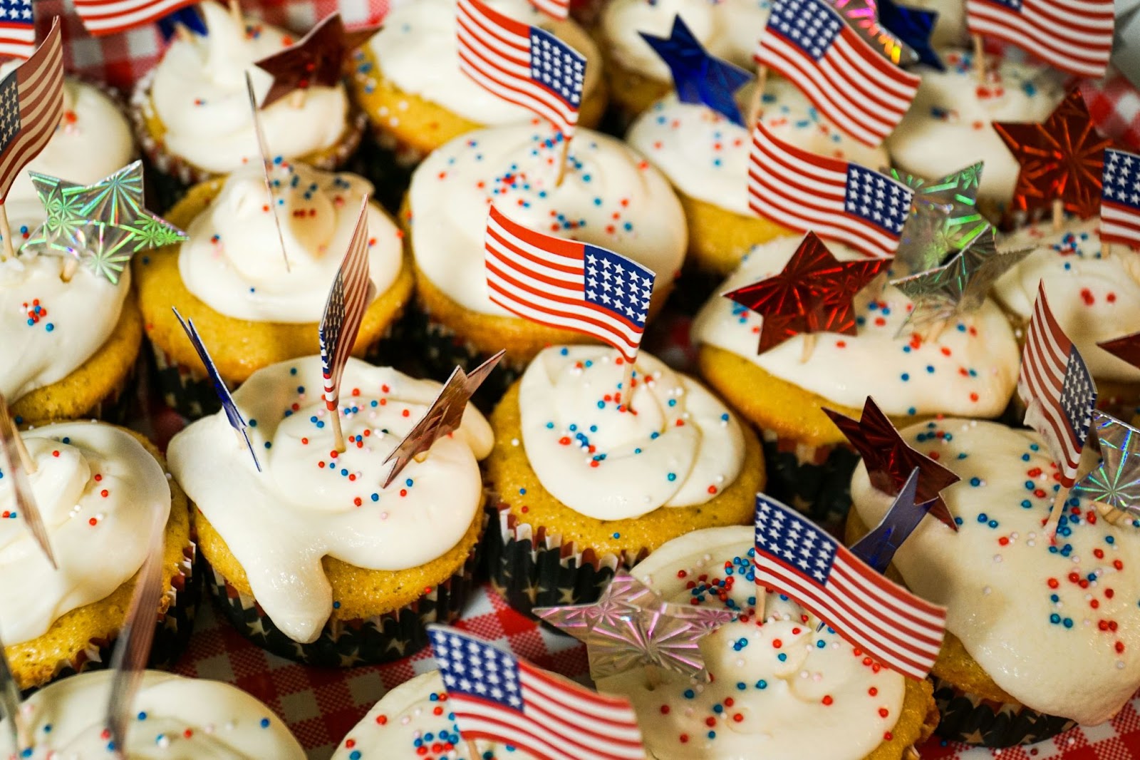 Cupcakes blancs avec un glaçage blanc et des pépites rouges, blanches et bleues, de petits drapeaux américains et des étoiles dépassant du haut de chacun.