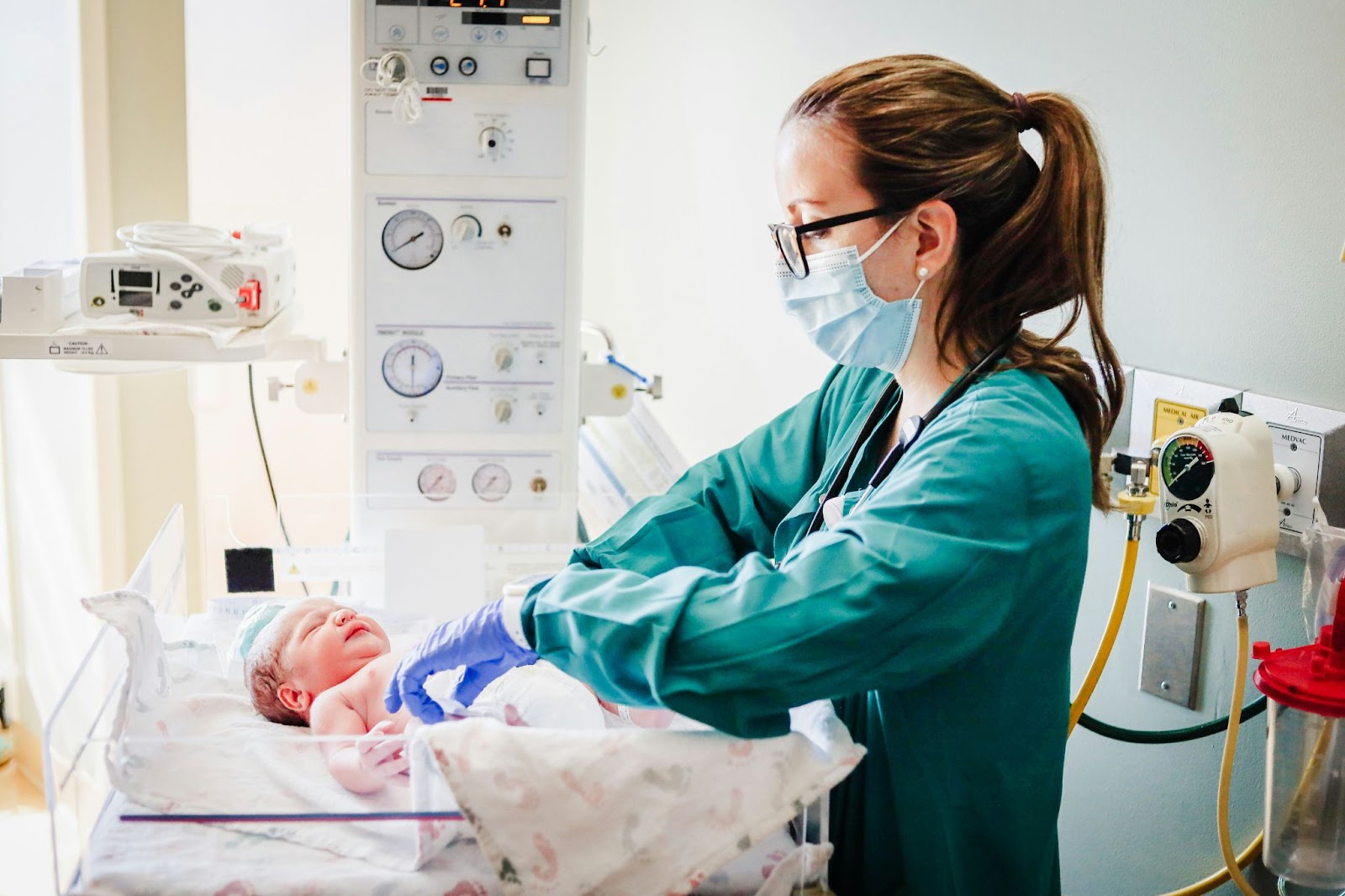 Una dottoressa o un'infermiera che indossa un camice, guanti e una maschera per controllare i segni vitali del neonato.