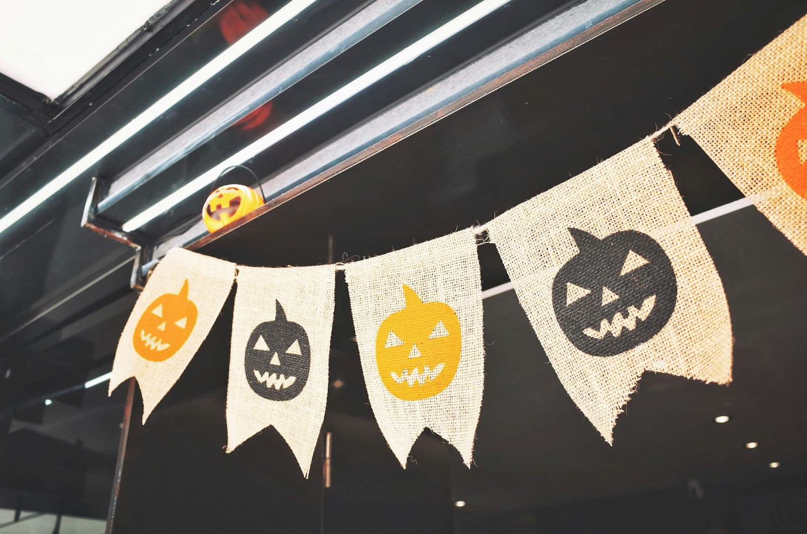 Banner de Tweed Halloween com lanternas pretas e laranja alternadas penduradas em um espaço industrial.