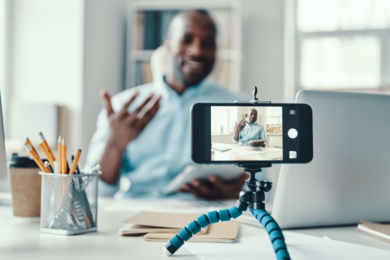 Homme enregistrant une vidéo de lui-même dans un bureau bien éclairé sur un iPhone.